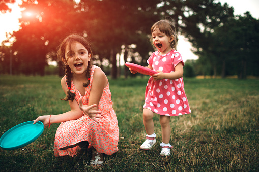 Portrait of two sisters on picnic playing frisbee. They are smiling and looking at camera.