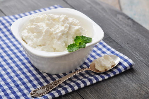 Ricotta cheese in bowl with mint on wooden background