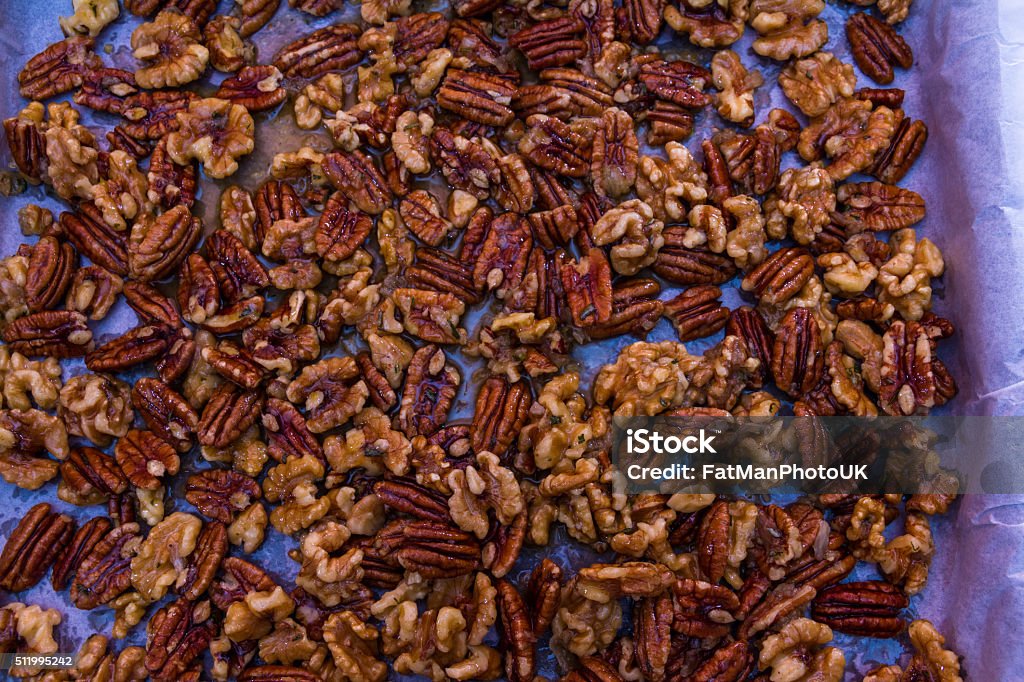 Mix nuts covered in butter garlic and rosemary mixture Preparing pecan nuts and walnuts in butter, water, garlic, rosemary, sugar ready for roasting on parchment in tray. Bar - Drink Establishment Stock Photo