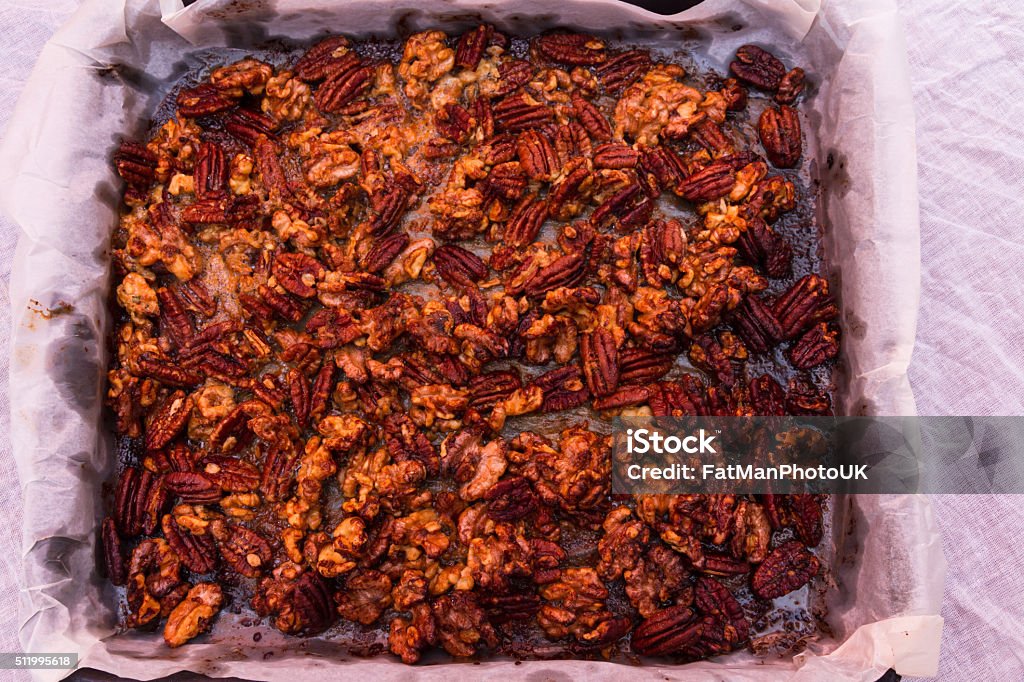 Mixed garlic and rosemary roasted nuts cooked and cooling Pecan nuts and walnuts roasted with garlic and rosemary on parchment in tray. Bar - Drink Establishment Stock Photo