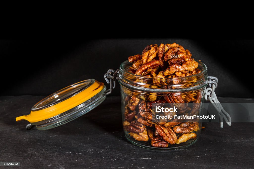 Jar with mixed garlic and rosemary roasted nuts. Pecan nuts and walnuts roasted with garlic and rosemary in jar. Dark background. Bar - Drink Establishment Stock Photo