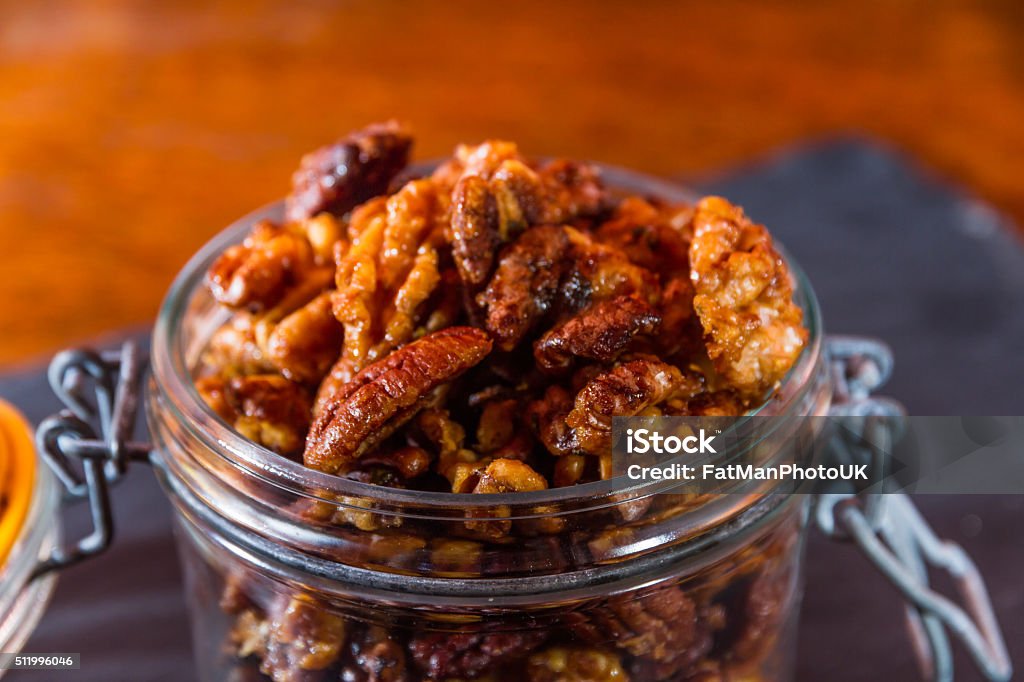 Bowl with mixed garlic and rosemary roasted nuts, macro. Pecan nuts and walnuts roasted with garlic and rosemary in ceramic bowl. Dark background, closeup. Bar - Drink Establishment Stock Photo