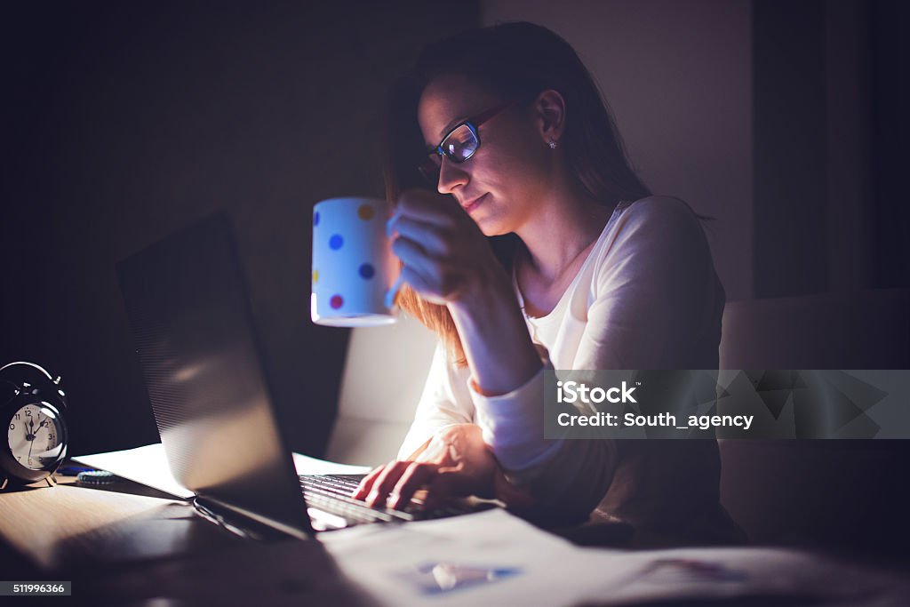 Tired Woman working at home,making a break Scene of a  young business woman working late at night to meet an urgent deadline,holding coffee Dark Stock Photo