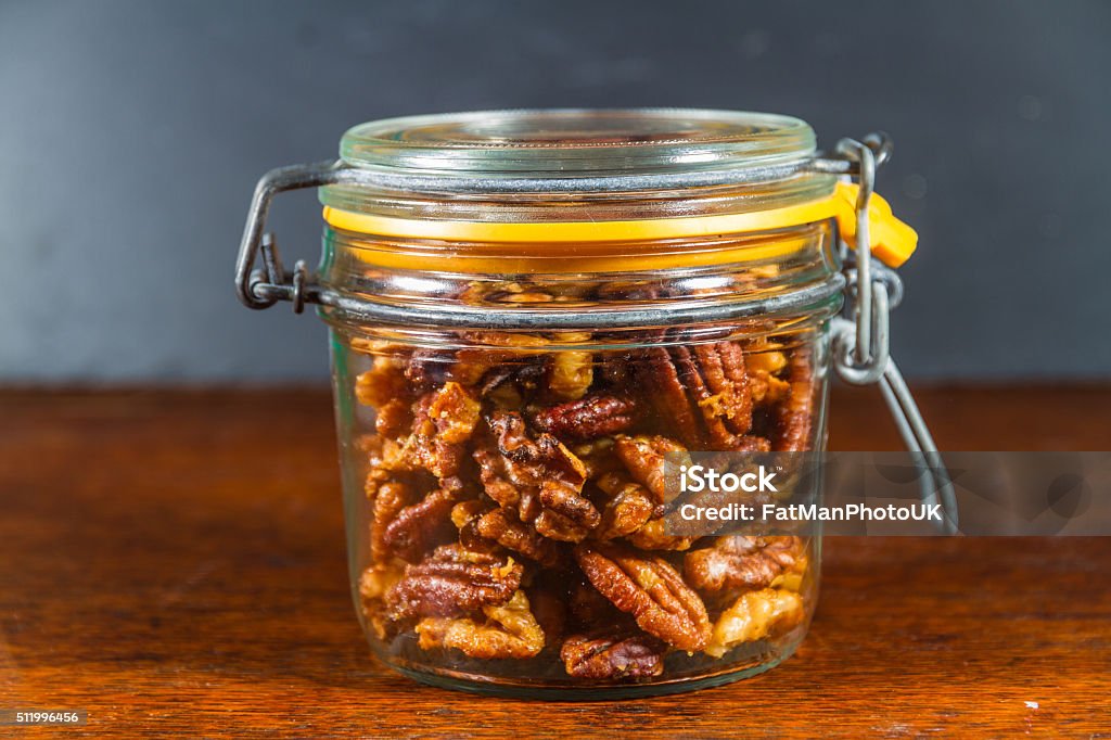 Jar with mixed garlic and rosemary roasted nuts. Pecan nuts and walnuts roasted with garlic and rosemary in jar. Dark background. Bar - Drink Establishment Stock Photo