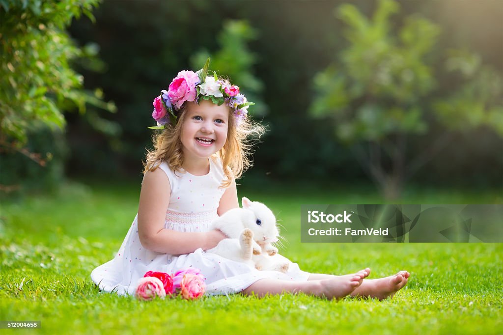 Little girl playing with real rabbit Girl playing with real rabbit in sunny garden. Child and bunny on Easter egg hunt in flower meadow. Toddler kid feeding pet animal. Kids and pets play.  Fun and friendship for animals and children. Animal Stock Photo