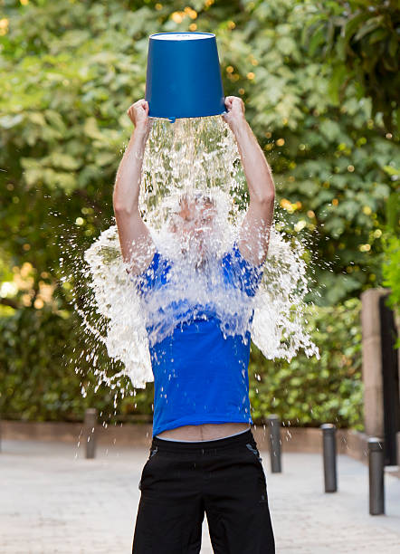 man pouring ice bucket on internet viral media campaign young man pouring ice water bucket on his head getting wet outdoors in internet viral media network challenge campaign to support degenerative sclerosis and neuronal disease and disorder bucket photos stock pictures, royalty-free photos & images