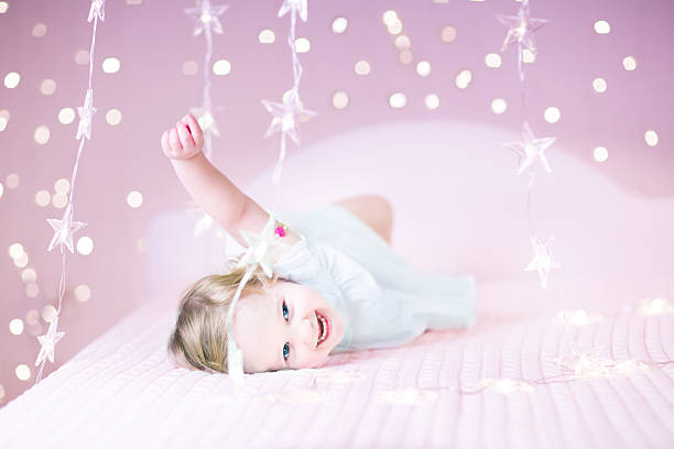 Happy laughing toddler girl playing on a bed between beautiful soft pink lights