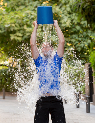 young man pouring ice water bucket on his head getting wet outdoors in internet viral media network challenge campaign to support degenerative sclerosis and neuronal disease and disorder