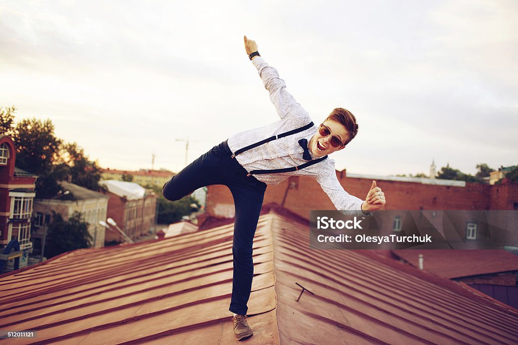 Young happy hipster girl jump on roof Young bold girl woman in hipster clothes, jumping on the roof, dressed like a boy man in a shirt, bow-tie, suspenders and pants trousers Adventure Stock Photo