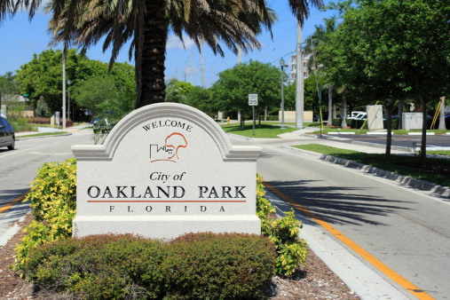 Oakland Park, Florida, USA - May 7, 2013: Cement sign with buildings and tree graphic welcoming people to the city of Oakland Park, Florida on a tropical foliage street median on a sunny blue sky day.