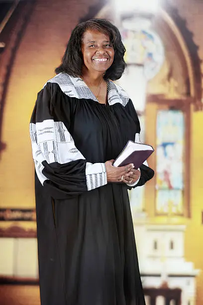 A  senior-adult woman in her black and white pastoral robe inside an old English Gothic church.