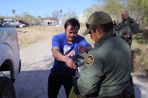 Rio Grande City, Texas, USA - February 9, 2016:  A Border Patrol agent collects belongings from a Mexican man while taking him into custody for illegally entering the U.S. by crossing the Rio Grande River in the Rio Grande Valley in far south Texas.  A continuous game of cat and mouse plays out along the river twenty four hours a day.