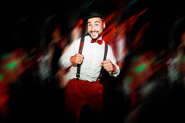 The groom dancing on dance floor, moving in motion. Cheerful man in hat, with mustache, beard and bow tie with suspenders. White shirt and red pants. Wedding color style Marsala. Having fun on party.