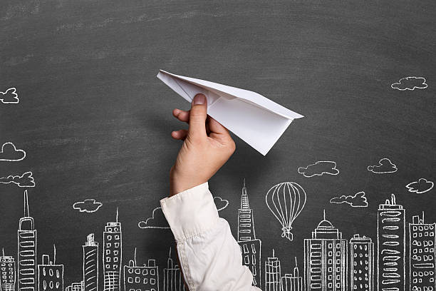 istock Child throwing white paper airplane against cityscape background 512041610