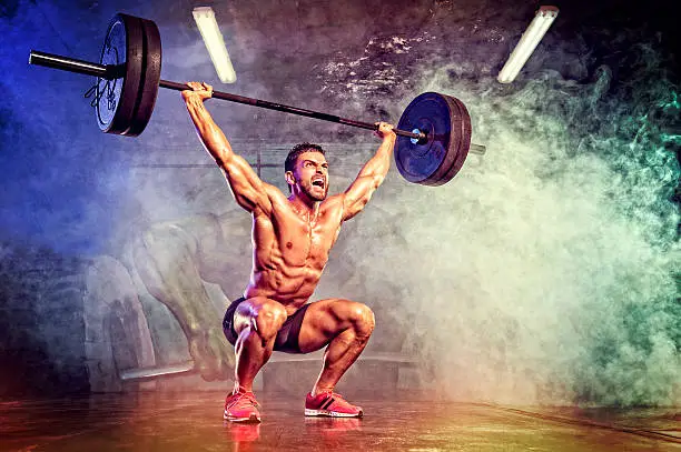 Athletic man doing Olympic styled weightlifiting (snatch) at a gym gym.
