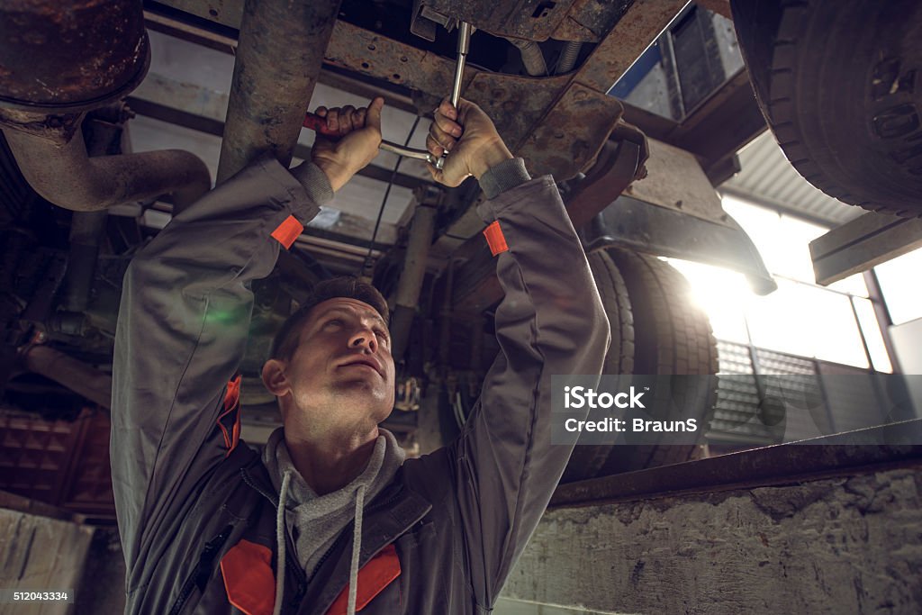 Auto mechanic working on a chassis of a truck. Mid adult mechanic using socket wrench while working on a chassis of a truck. Truck Stock Photo