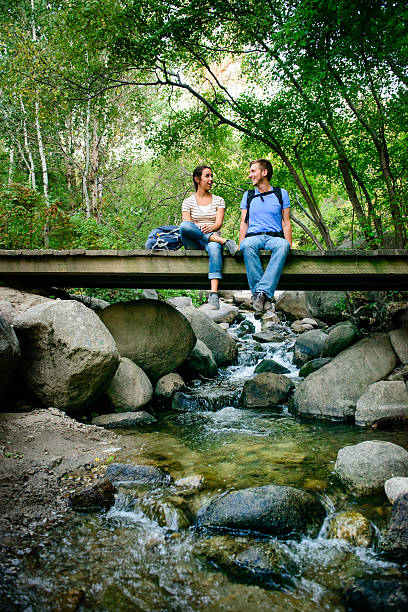Couple talking to each other while they sit on a bridge over a stream in the mountains.