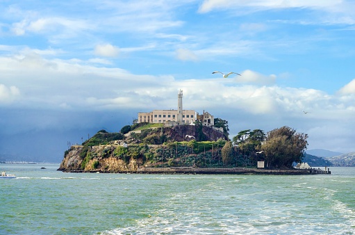 The Alcatraz Penitentiary, now a museum, in San Francisco, California, United States of America. A view of the island, the lighthouse, prison buildings and the San Francisco Bay from the coast on a sunny day.