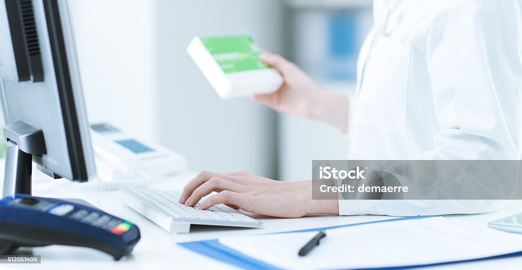 Pharmacist searching products in the database Pharmacist holding a medicine packet and searching that product in the computer database, healthcare and technology concept Pharmacy Stock Photo