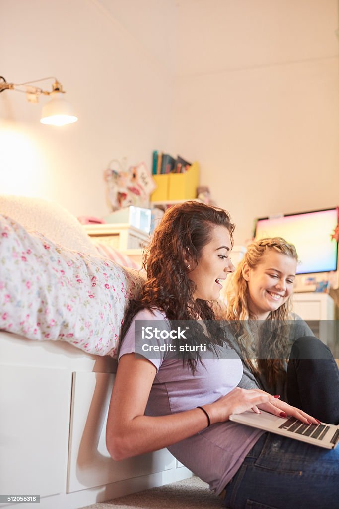 two young women online tow friends sit on the floor of a bedroom laughing at a laptop. they could be students or maybe just social networking friends . They are having fun . 18-19 Years Stock Photo