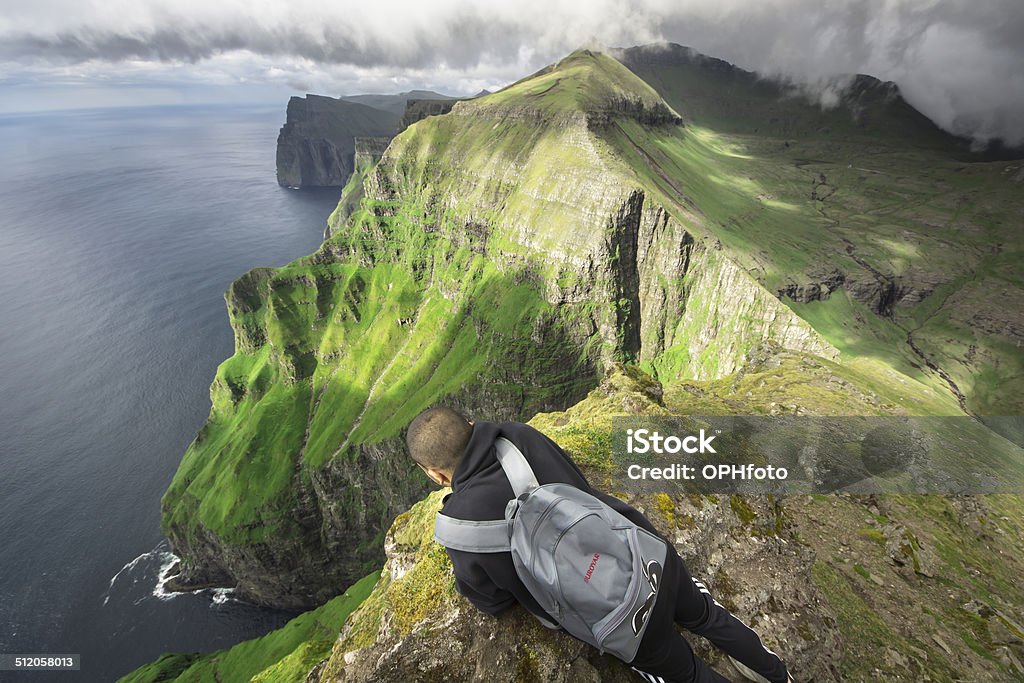 Watching Nature A man sitting on the top of a mountain and watching the beautiful nature. Faroe Islands Stock Photo