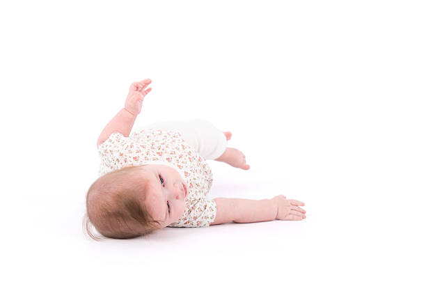 Baby development. Studio shot, full length of 6 months old baby girl lying on back trying to roll over. Isolated on white background image. half dressed girls pictures stock pictures, royalty-free photos & images
