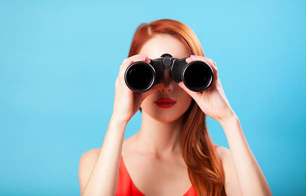 Redhead girl with binocular on blue background. stock photo