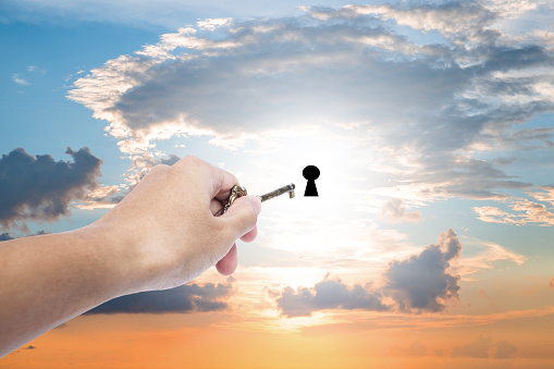 Hand holding golden key extending to unlock on sunset sky, business abstract concept