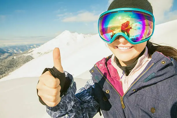 Happy girl dressed in ski or snowboard fashion mask goggles. Successful gesture thumbs up. Mountain landscape. Extreme adventure. Winter ski resort