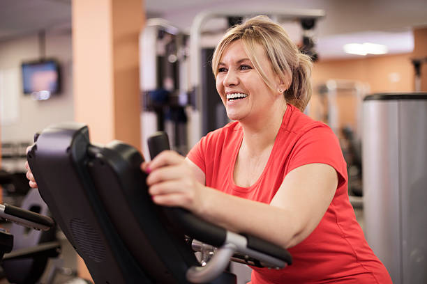 szczęśliwa kobieta jazdy na rower treningowy na siłowni - gym zdjęcia i obrazy z banku zdjęć