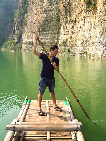 Man floating on a bamboo raft on the green water of lake, Shidu, China. Shidu conservation area is one of the most beautiful places with unique nature in China.