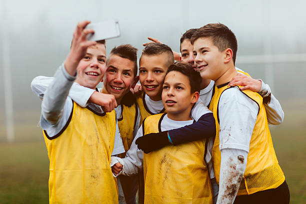 Kids Making Selfie After Playing Soccer. Children playing soccer. They are having training on foggy, cold, winter morning. They are dedicated to become a new soccer stars. Making selfie with smart phone after training or game. They are smiling and they are dirty with mud. mud photos stock pictures, royalty-free photos & images