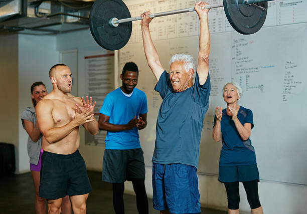 Impossible is nothing Shot of a senior man lifting weights while a group of people in the background watch onhttp://195.154.178.81/DATA/i_collage/pu/shoots/806425.jpg Barbell stock pictures, royalty-free photos & images
