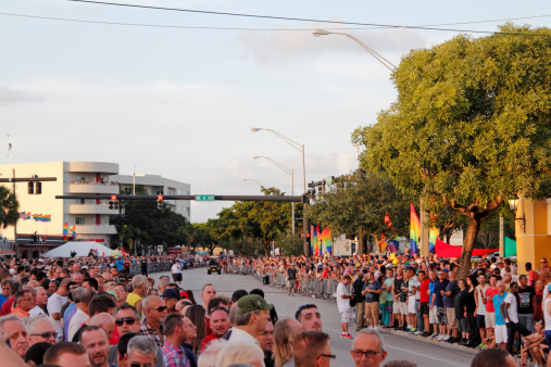 Wilton Manors, Florida, USA - June 22, 2013: Many people waiting for the LGBT pride parade on the sides of colorfully decorated with rainbow flags Wilton Drive in the evening just before a golden sunset.