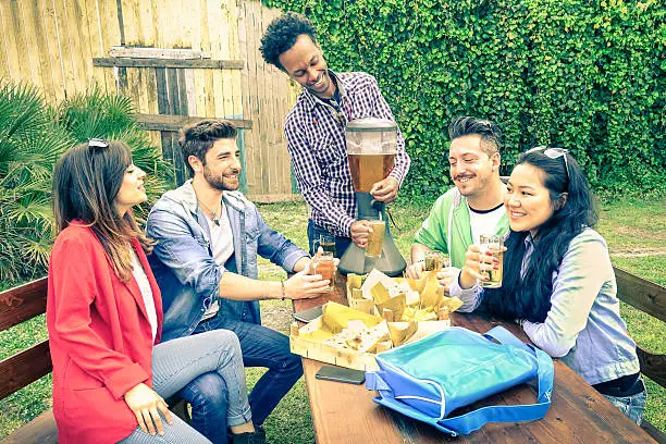 Photo of Multiracial happy friends eating and toasting at bbq garden party
