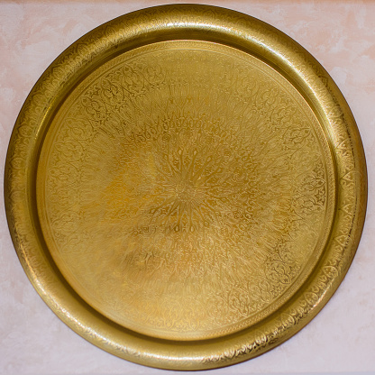 Ornate engraved round brass wall plaque mounted on a white wall with a geometric repeat pattern, close up view