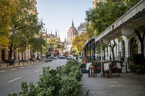 Street of Budapest with view at the Hungarian Parliament Street of Budapest with a pavement cafe and a view at the Hungarian Parliament Building on a bright autumn day budapest stock pictures, royalty-free photos & images