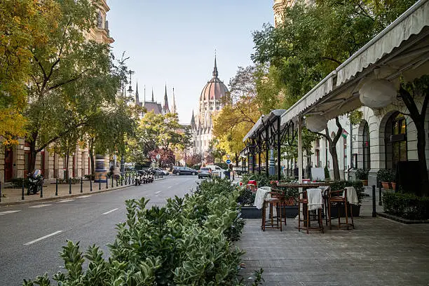 Street of Budapest with a pavement cafe and a view at the Hungarian Parliament Building on a bright autumn day