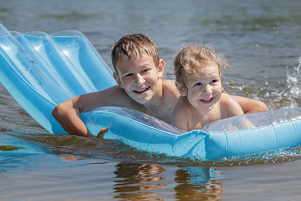 duas crianças desfrutando de nadar com colchão de ar na piscina inflável - child inflatable raft lake family - fotografias e filmes do acervo