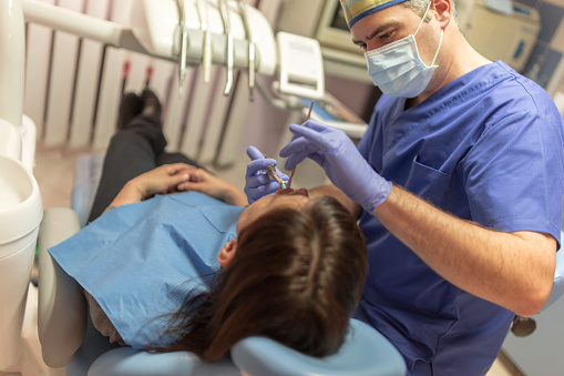 With a help of a dental assistant, male Caucasian dentist, performing oral exam on female patient, at the dentist's office