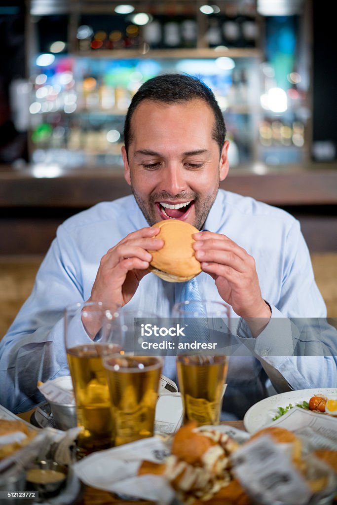 Man eating a burger at a bar Happy man eating a burger at a bar or pub - food and drinks concepts Adult Stock Photo