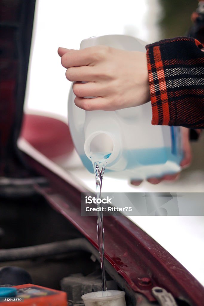 Pouring Antifreeze Washer Fluid into Windshield Washer Tank Closeup shot of hands holding bottle with antifreeze washer fluid and pouring it into windshield washer tank in winter day. Bottle Stock Photo