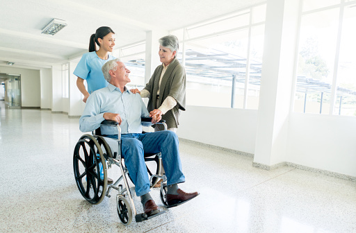 Nurse pushing senior man in a wheelchair at the hospital and talking to his wife - adult care concepts