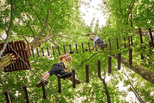 photo of two friends in adventure park enjoying summer day while climbing suspension bridge.
