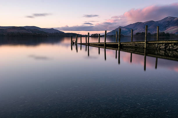 Jetty Reflections In Calm Lake With Pink Clouds In Sky.