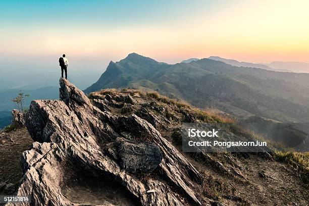 Hombre Caminatas En El Pico De La Montaña De Rocas Al Anochecer Foto de stock y más banco de imágenes de Montaña