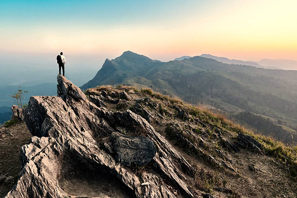 businessman hike on the peak of rocks mountain at sunset - 石材 圖片 個照片及圖片檔