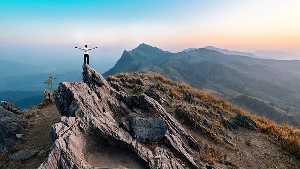 businessman hike on the peak of rocks mountain at sunset stock photo