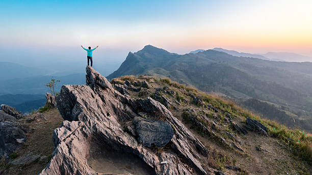 Man Hike on the peak of rocks mountain at sunset stock photo