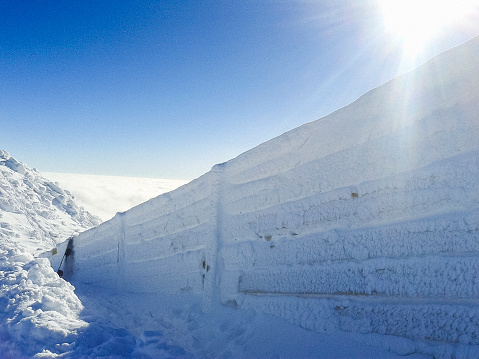 Winter is coming. Snow-covered and ice-covered wooden fence with sun on the blue sky behind the wall. Mountains view, Europe.